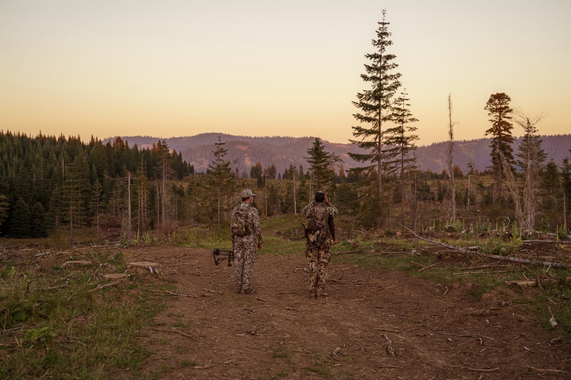 Two hunters walking a trail at sunset with mountain forest backdrop